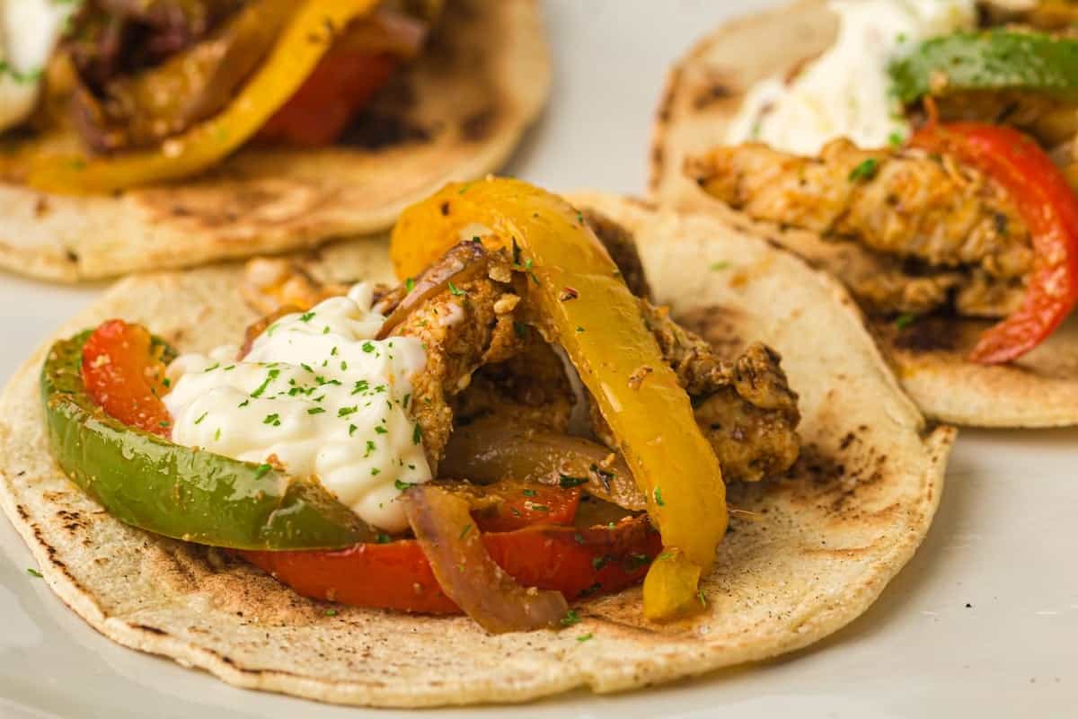 A wooden board with seasoned chicken wings, a bowl of white dipping sauce with lemon slices, and celery and carrot sticks.