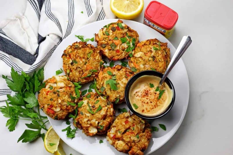 Overview of air fryer crab cakes with a sauce on a white background.