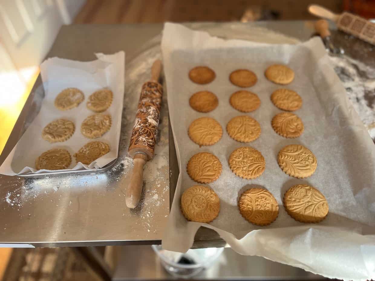 Eight embossed round cookies on a parchment-lined baking sheet. The cookies feature intricate floral and leaf patterns.