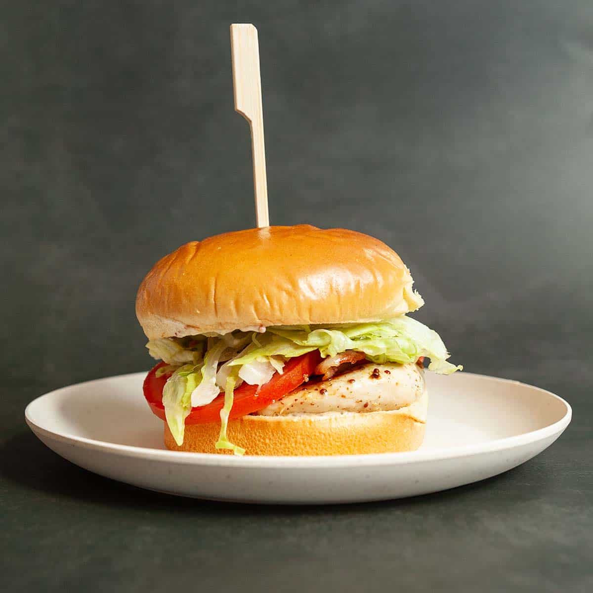 A chicken and bacon sandwich on a brioche bun with lettuce and tomato.