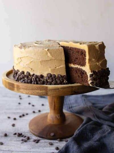 Chocolate and peanut butter cake on a wooden cake stand with a slice cut.