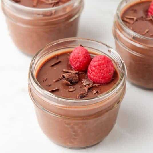 Chocolate custard in a jar topped with raspberries and shaved chocolate.
