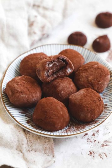 Chocolate truffle mochi stuffed with truffles covered in cocoa powder on a plate with a piece showing the truffle inside.