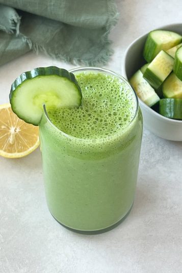 Cucumber smoothie in a tall glass with a cucumber slice over the rim.