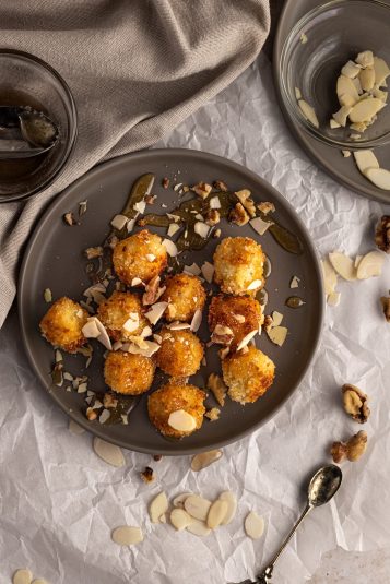 Goat cheese croquettes drizzled with honey, almonds and walnuts, on a dark grey plate.