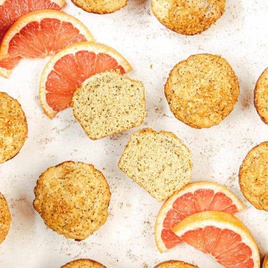 Grapefruit poppy seed muffins on a table with slices of fresh grapefruit.