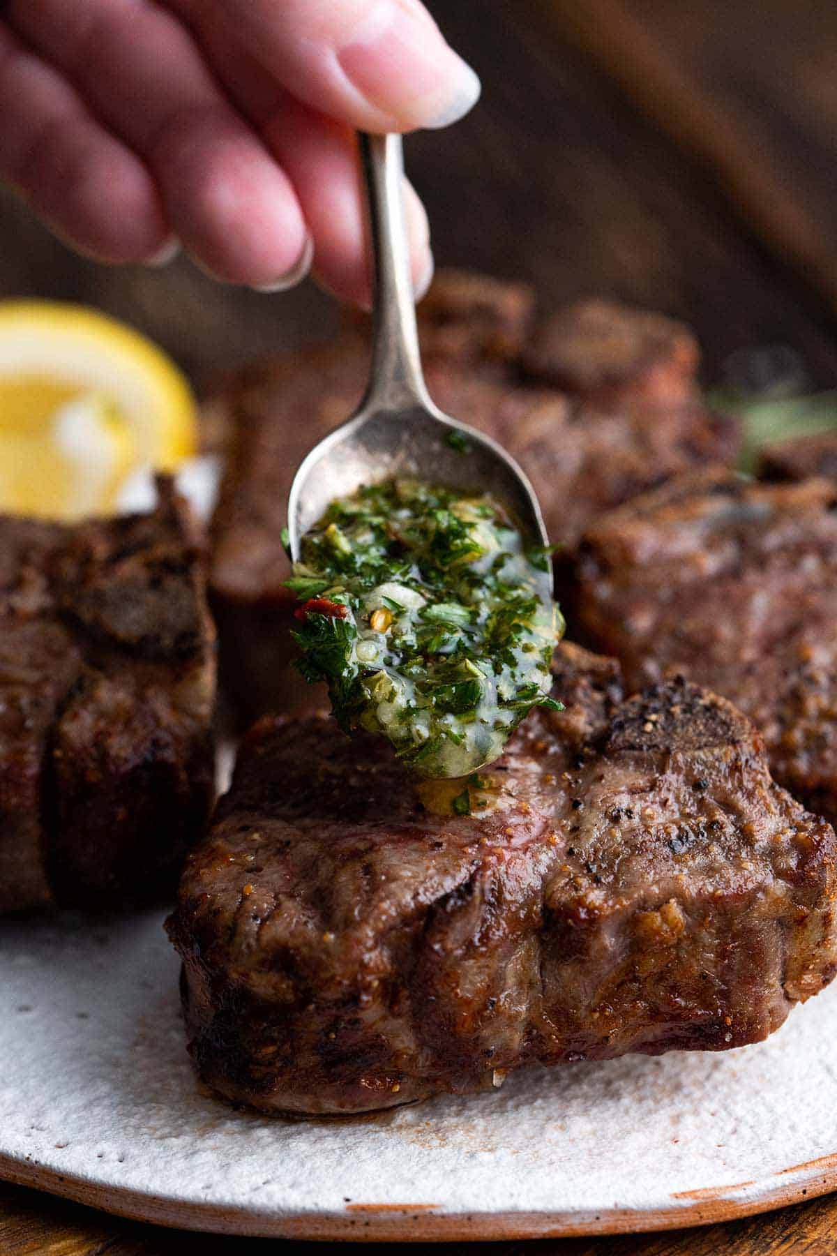 Hand spooning fresh garlic herb sauce eon top of cooked lamb chops.