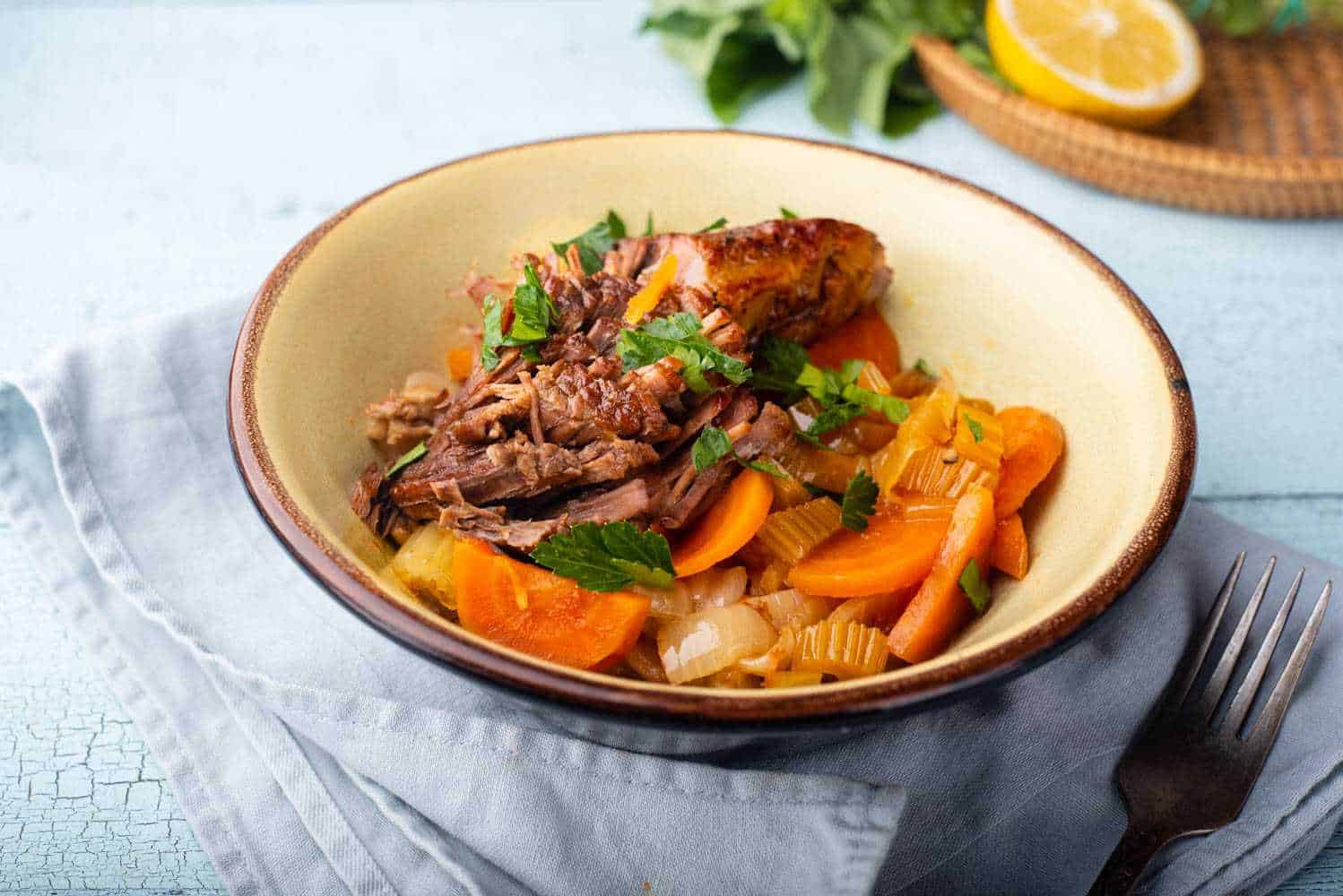 Beef brisket with sliced carrots, onion, celery and parsley in white bowl.