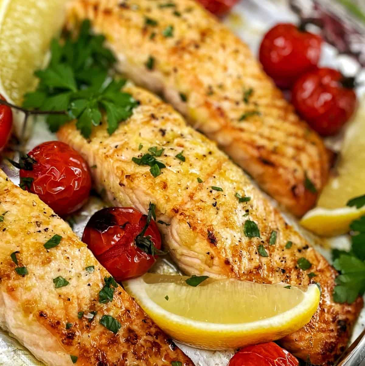 Cooked salmon fillets on a baking tray with lemon tomatoes and parsley.