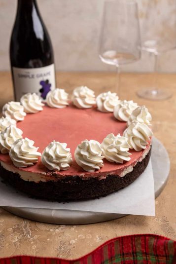 A no bake red velvet cheesecake with dollops of whipped cream on a marble cake stand.