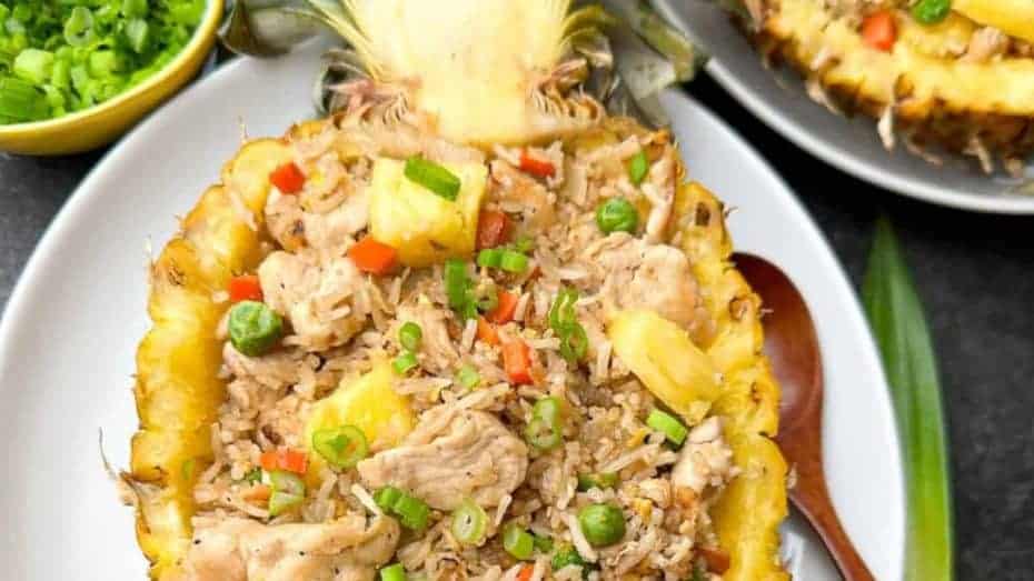 Pineapple half filled with chicken fried rice, peas, and diced red peppers; garnished with green onions.