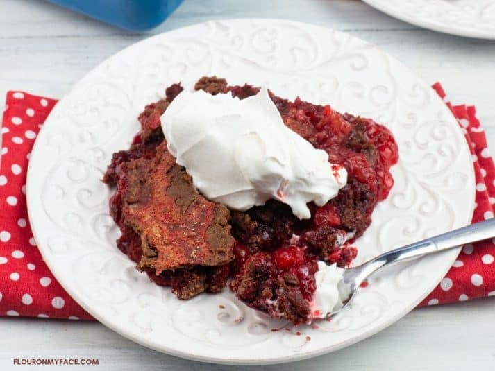 Serving red velvet dump cake topped with whipped cream on a dessert plate.