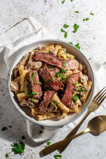 A bowl of creamy steak pasta on a white background.