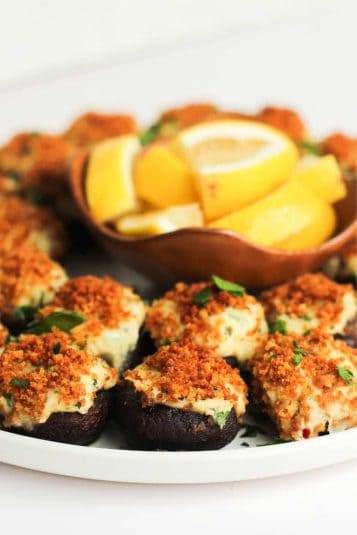 Stuffed mushrooms with crab on a white plate and a bowl with lemon wedges.