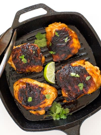 Blackened chicken thighs in grill pan with cilantro and lime wedge.