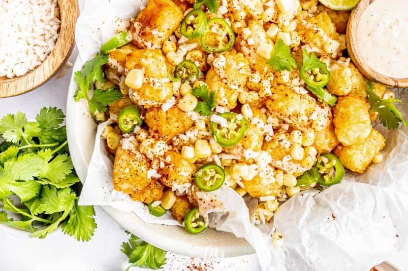 Mexican street corn over tater tots in a white bowl.