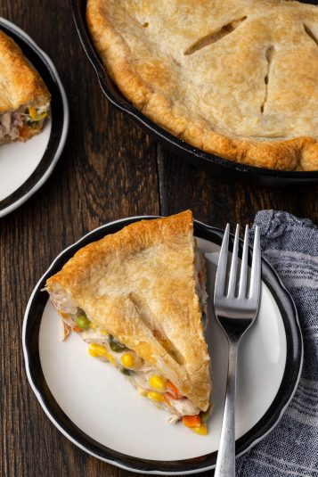 A slice of chicken pot pie on a plate next to the chicken pot pie in a skillet.