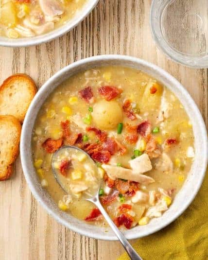 A bowl of chicken corn chowder topped with bacon and chives sitting on a wood table.