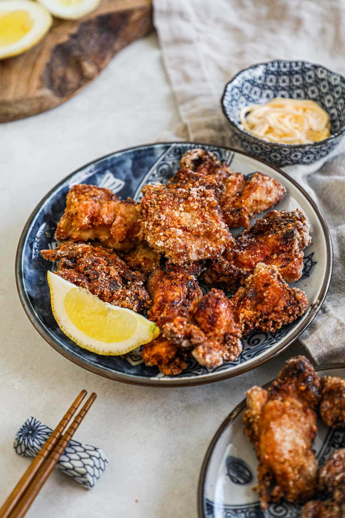 Crispy karaage chicken on a blue Japanese porcelain plate with a lemon wedge, chopsticks, and a small bowl of Kewpie mayo for dipping.