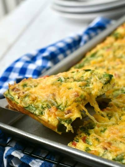 A square of sheet pan omelet being pulled from the pan with cheese pulling as its lifted.