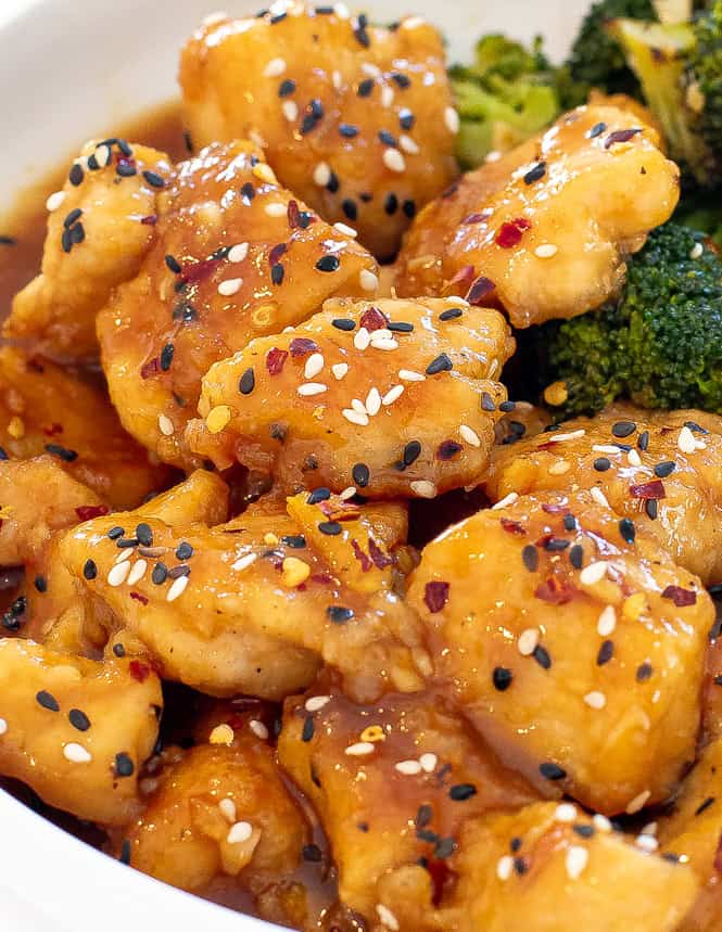 Slow cooker orange chicken topped with sesame seeds and crushed red pepper flakes.