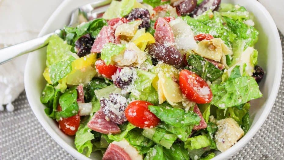 A slice of whole-grain bread with avocado spread topped with two tomato slices and garnished with chopped cilantro on a white square plate.