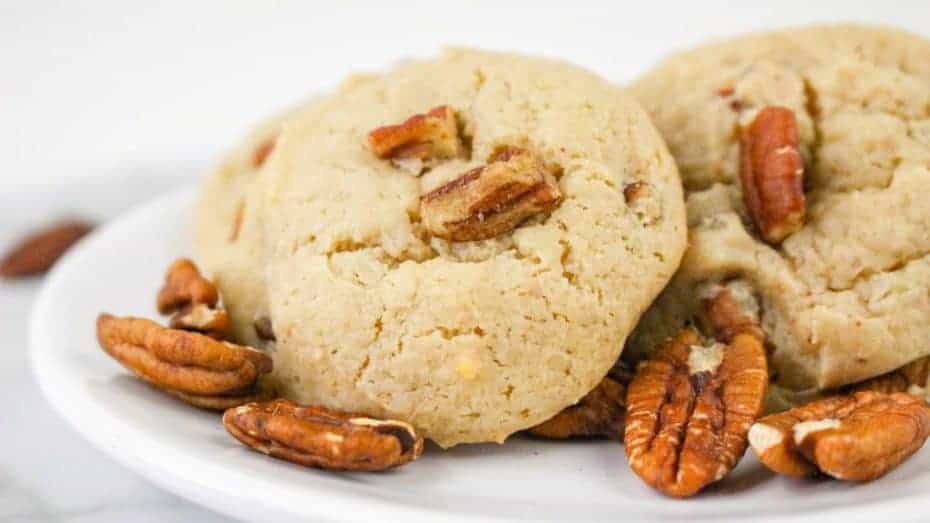 Pecan cookies on a white plate, surrounded by pecan halves.