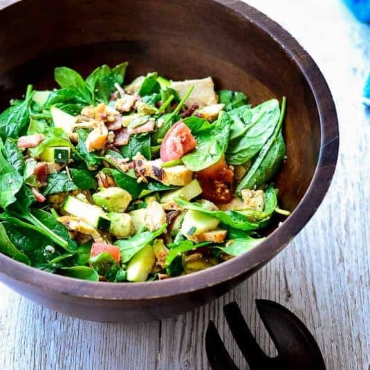 An overhead shot of a wooden serving bowl filled with salad next to cornbread on a cutting board.