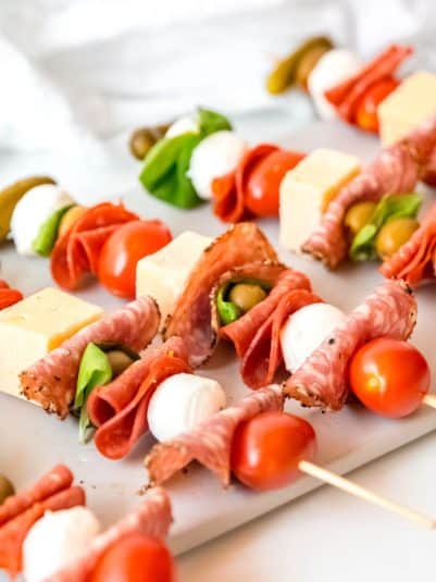 Meat and cheese charcuterie sticks with olives, tomatoes, and basil layered in.