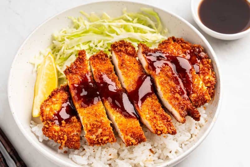Plate of Chicken Katsu with drizzle of tonkatsu sauce, rice and shredded lettuce.