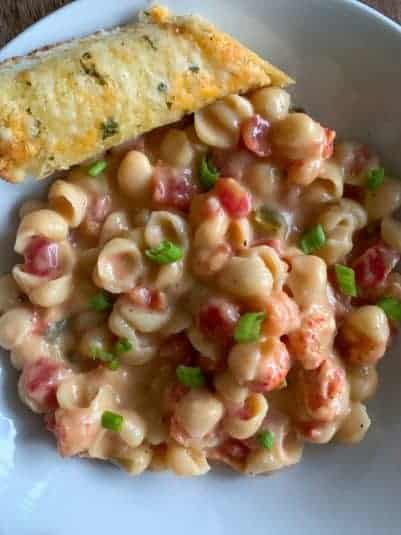 Mac and cheese with crawfish and piece of garlic bread on white bowl.