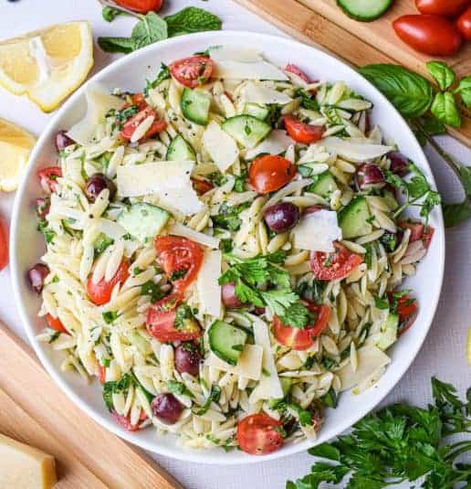 Bowl filled with lemon orzo pasta salad with cucumbers, tomatoes, olives, parmesan cheese and fresh herbs.