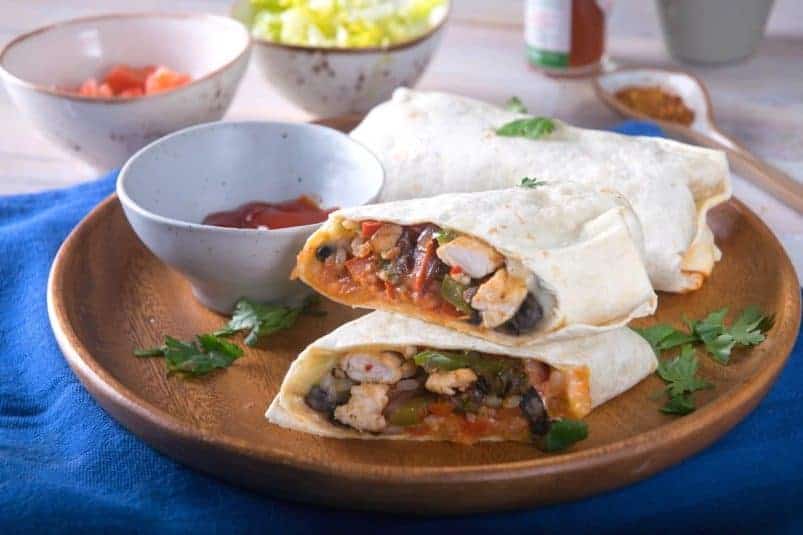 Kimchi burritos on wooden circular serving plate with a bowl of red sauce.