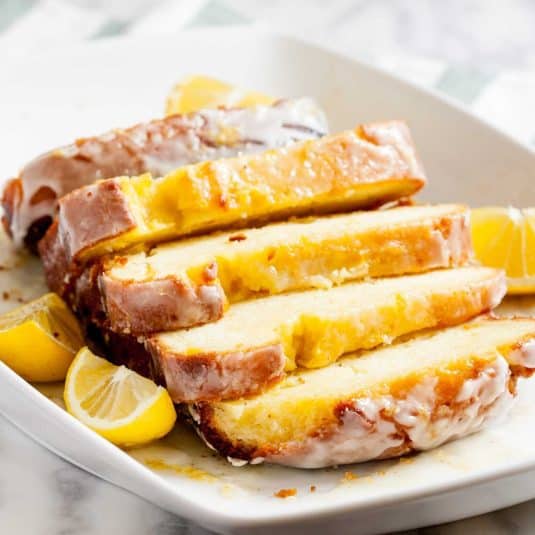 A slice of layered lemon icebox cake with graham cracker crust and whipped cream topping, drizzled with lemon curd.