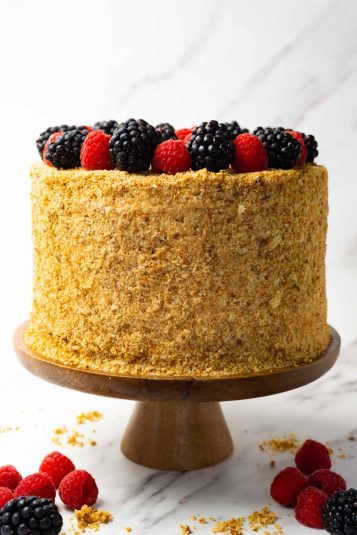 A freshly made napoleon cake dusted with the cake crumbs and fresh raspberries and blackberries served on a wooden cake stand.
