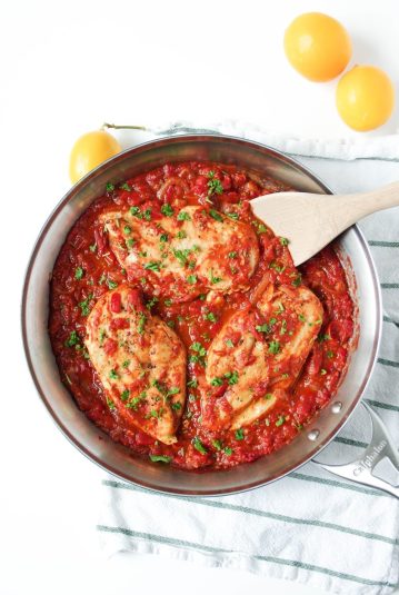 Large skillet filled with homemade roasted red pepper sauce and three whole chicken breasts garnished with chopped parsley.