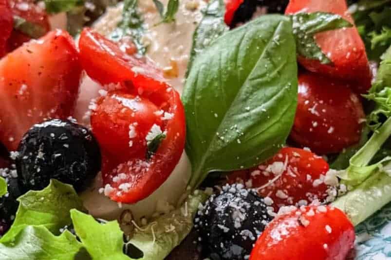 A fresh salad with sliced apples, pecans, and mixed greens on a white rectangular plate. The apples have a red peel and are thinly sliced, while the greens provide a leafy background, creating a colorful and healthy dish.