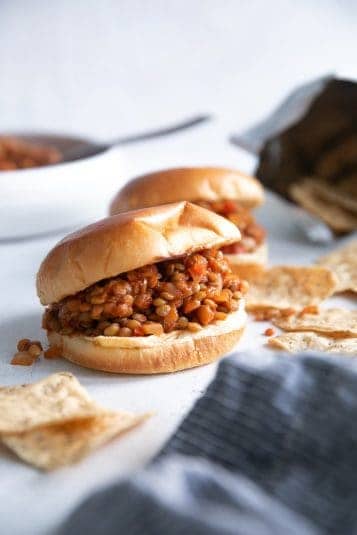 Two lentil sloppy joes served on a brioche bun with a side of chips.