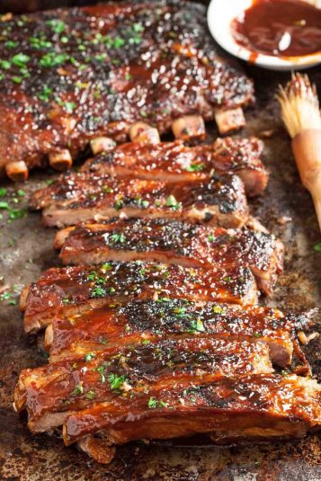 A platter of tender oven-baked BBQ ribs garnished with herbs on a rustic surface.