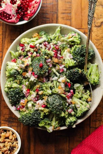 Broccoli pomegranate salad in a white bowl on a wooden surface.