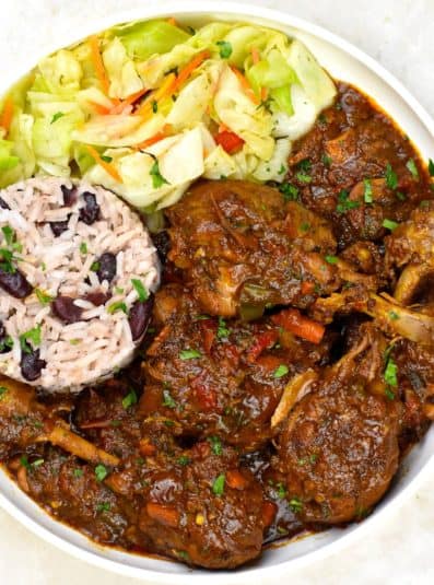 Serving of Jamaican chicken stew in a bowl with rice and cabbage.