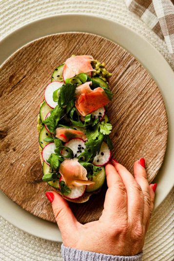 Top view of a hand holding avocado toast on a plate.