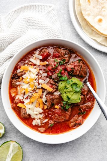 A bowl of Instant Pot enchilada soup in between sliced limes and tortillas.