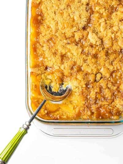 The bottom left corner of a 9x13 baking dish of peach cobbler with a serving spoon with a green handle sticking out of the dish.