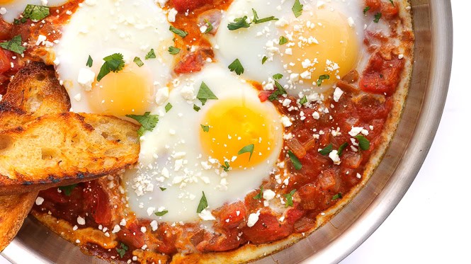 Overhead shot of author dipping grilled baguette into Shakshuka recipe.