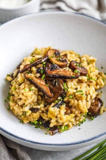 Truffle mushroom leek risotto in a bowl with sautéed crimini and shiitake mushrooms on top.