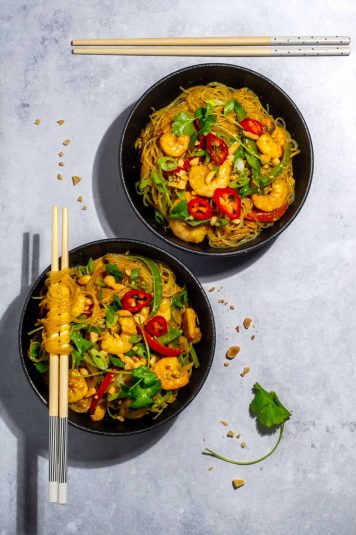 Two bowls of prawns with noodles on a light background with chopsticks.