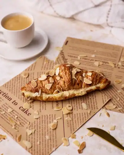 Almond croissant on some brown paper next to a small cup of espresso.