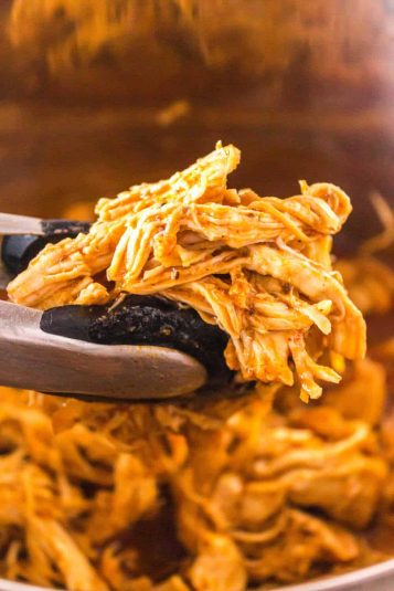 Tongs that are holding bbq shredded chicken.