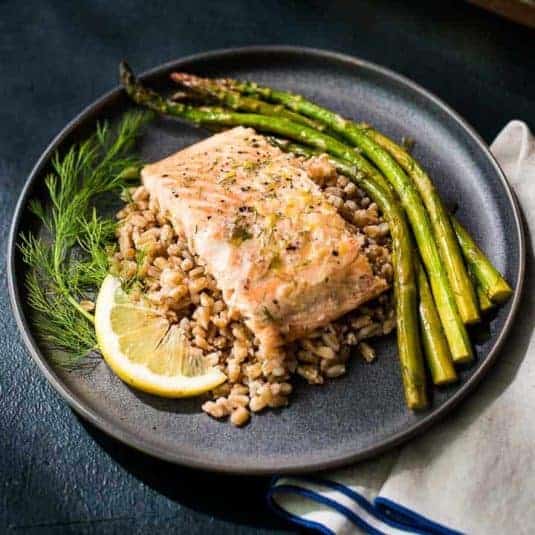 Hands holding a baking dish with Lemon Dill Salmon and Asparagus.